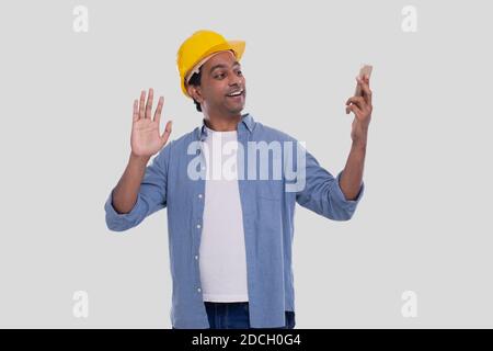 Addetto alla costruzione che ha una videochiamata al telefono. Telefono di tenuta ARCHITECT. Elmetto rigido giallo. Uomo isolato parlando al telefono. Uomo che ha un video Foto Stock