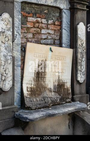 Un'antica lapide con nomi e date incisi, appoggiata a un muro di mattoni in rovina a New Orleans, Louisiana Foto Stock