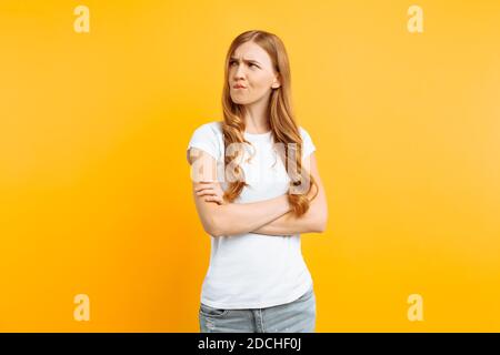 Ritratto di una giovane ragazza capovolto, in una T-shirt bianca, in piedi con le mani piegate e il volto offeso, su uno sfondo giallo Foto Stock