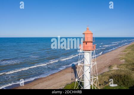 Vista aerea del faro con parte superiore rossa e base bianca. Cielo blu e mare. Faro di Pape Foto Stock