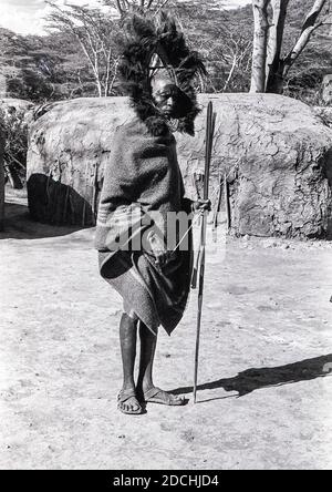 Kenya. Si tratta di un capo anziano Maasai all'incontro annuale della popolazione tribale Maasai nella Rift Valley, non lontano dalla piccola città di Narok, Quando i giovani Maasai Moran i cosiddetti guerrieri sfilano e ballano in uno dei villaggi nella speranza di attrarre alcune giovani ragazze come futura moglie. La lancia è puramente cerimoniale come il suo capo-vestito di piume Ostrich. Inoltre fornisce l'occasione affinchè il womenfolk visualizzi e possibilmente vendano alcune delle loro opere d'arte distintive. La casa ancestrale di Maasai è la Rift Valley, che costituisce il famoso Parco Nazionale Maasai Mara e la Riserva del gioco. Foto Stock