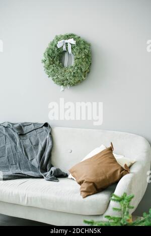 Elegante soggiorno minimalista con divano con cuscini e. Una corona di Natale sulla parete grigia Foto Stock