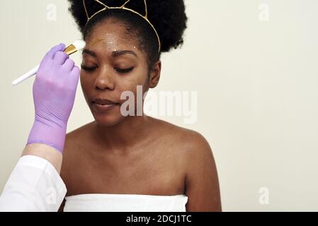 Trattamenti di bellezza Spa, cura della pelle. Donna che ottiene la cura del viso da estetista al salone del centro benessere. Giovane cosmetologo applicando maschera facciale a pennello in spa. Foto Stock