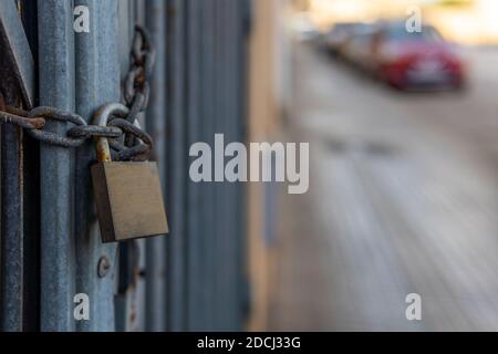 Recinzione di un'azienda chiusa con una catena e una serratura. Sullo sfondo una strada urbana non focalizzata con bokeh Foto Stock