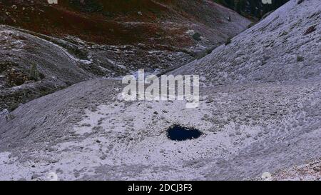 Vista aerea di una valle con prati innevati e un piccolo stagno a forma di cuore nelle montagne alpine di Montafon, Alpi, Austria in autunno. Foto Stock