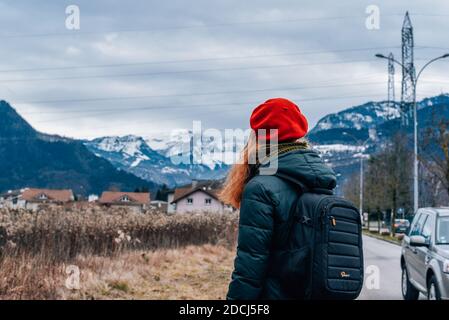 una ragazza con uno zaino e un beretto rosso guarda in montagna Foto Stock