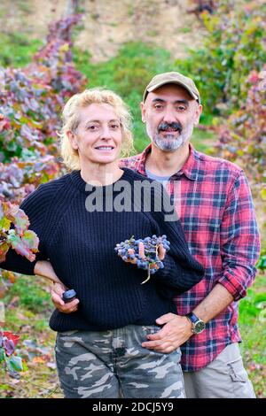 Giovane coppia matura di contadini in un vigneto con un mazzo di uve. Foto Stock