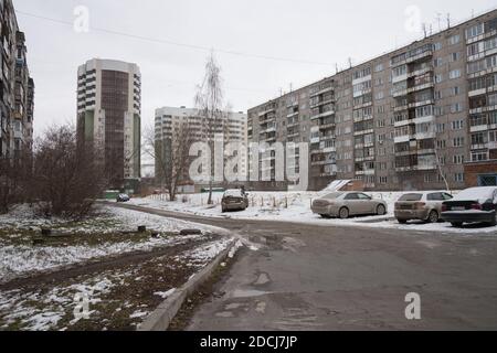 Una strada asfaltata conduce tra edifici di appartamenti con auto parcheggiate in una tipica zona residenziale di ​​Novosibirsk in inverno. Foto Stock