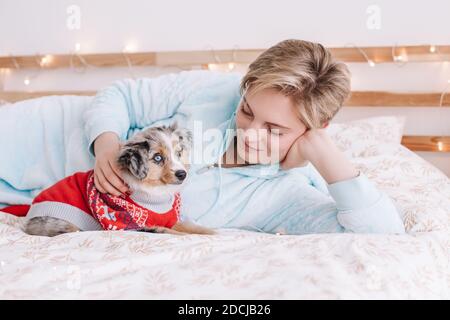 Giovane donna caucasica con capelli corti sdraiati a letto con simpatico cane cucciolo a casa. Il proprietario del PET accarezza il piccolo amico di furry. Rapporto di domest Foto Stock