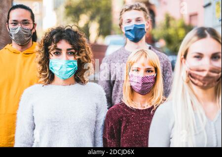 Gruppo di amici che cammina in città in tempo di coronavirus - nuovo concetto di camminata normale con i giovani coperti da maschera protettiva - fuoco sulle due ragazze vicino Foto Stock