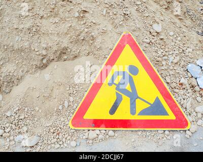 Cartello stradale triangolare rosso-giallo con immagine di uno scavo l'uomo si trova vicino a un mucchio di sabbia Foto Stock