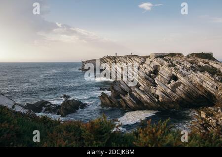 Una bella foto di una costa coperta da cespuglio con formazioni rocciose inclinate in arenaria a Peniche, Portogallo Foto Stock