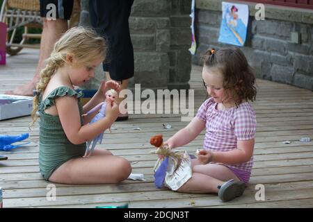 Due graziose ragazze caucasiche che si siedono su un portico giocando con le bambole Elsa e Anna dal movimento congelato. Foto Stock