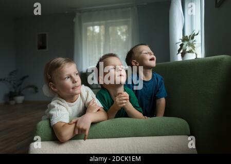 Bei bambini che si stendono sul divano a casa guardando fuori dalla finestra. Foto Stock