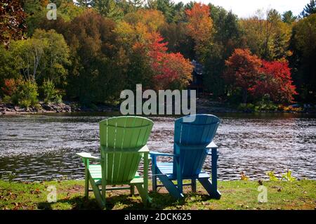 Due sedie Adirondack seduta su una riva del fiume con alberi sullo sfondo Foto Stock