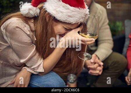 giovane femmina caucasica che tiene un bicchiere di vino bianco, che muore ridendo, o piangendo, con il cappello di santa Foto Stock