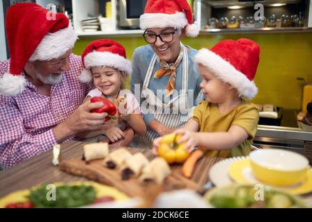 Nonno, nonna e nipoti in cucina insieme in un'atmosfera allegra gustando la preparazione di verdure per un pasto di Natale. Natale, famiglia, Foto Stock