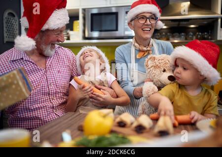 Nonno con i nipoti che si divertono a preparare il pasto di Natale insieme in un'atmosfera festosa in cucina. Natale, famiglia, insieme Foto Stock