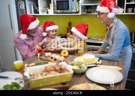 Nonno, nonna e nipoti preparano insieme il pasto di Natale in cucina in un'atmosfera allegra. Natale, famiglia, insieme Foto Stock