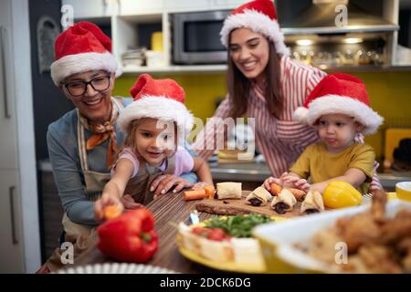 I bambini si divertano a preparare un pasto di Natale con la nonna e la madre in un'atmosfera festosa. Natale, famiglia, insieme Foto Stock