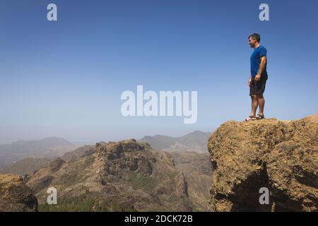 Escursionista impavido che guarda l'orizzonte dalla cima della scogliera a Roque Nublo, Gran Canaria. Avventuriero su una montagna rocciosa che contempla viste panoramiche Foto Stock