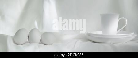 tazza bianca di ceramica e cibo di uovo ancora vita su morbido sfondo banner in tessuto Foto Stock