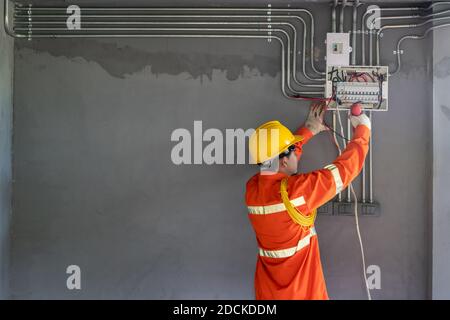 Elettricista asiatico indossare abiti di sicurezza con viti elettriche e fili sul sistema di protezione relè. Foto Stock