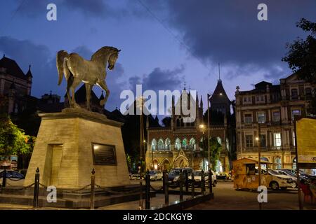 Il Monumento del Cavallo Nero nella zona di Kala Ghoda, Fort, Mumbai, India, al crepuscolo serale; b/g: Biblioteca di SASSOON Foto Stock