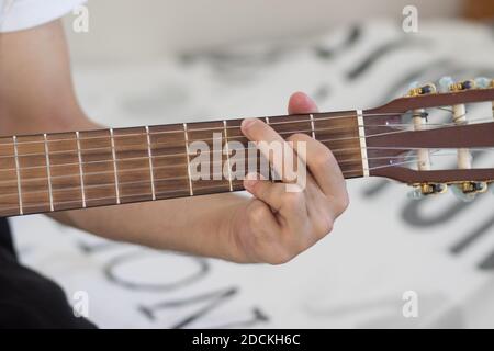 Un uomo che suona una chitarra classica spagnola, un primo piano sulla mano sinistra, uno sfondo sfocato Foto Stock