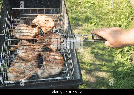 Primo piano di una mano dell'uomo che prepara carne fritta, all'aperto, in estate, sullo sfondo dell'erba Foto Stock