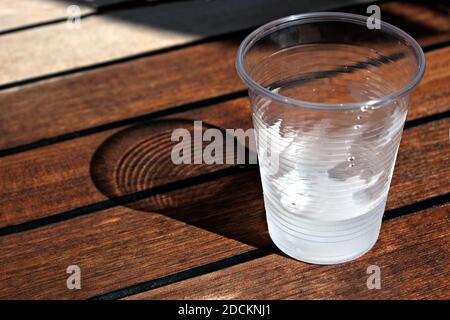 Vista ravvicinata di un vetro di plastica con acqua fredda un tavolo di legno Foto Stock