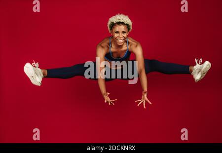 Donna allegra che fa l'allenamento. Atleta afroamericana che salta in aria e si allunga le gambe. Foto Stock