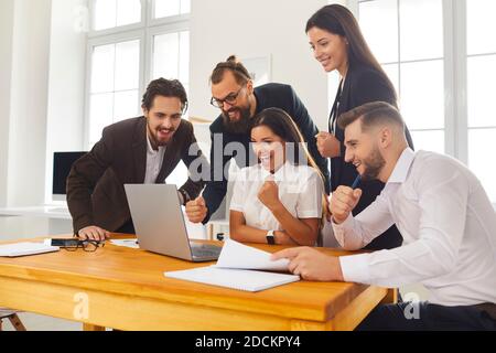 Team di colleghi entusiasti che guardano lo schermo del notebook per festeggiare il successo vendite Foto Stock