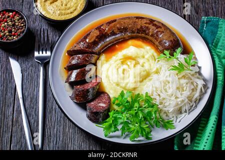 Cibo tedesco: Blutwurst o salsiccia di sangue servita su un piatto con crauti, purè di prezzemolo di patate, senape, e peppercorn su un tavolo di legno scuro, top Foto Stock