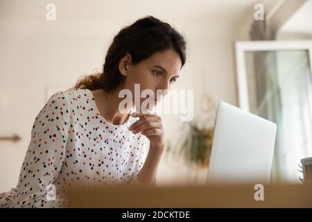 Una giovane donna attenta lavora su un computer portatile da casa Foto Stock