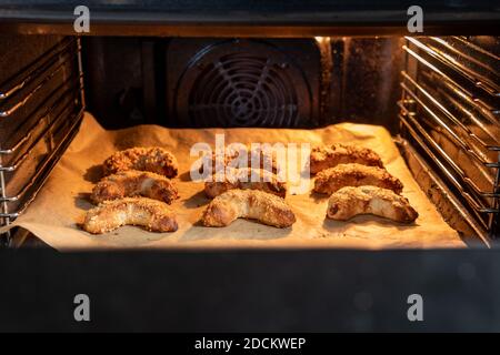 Deliziosi croissant di mandorle vegane appena sfornati con mandorle tritate su una griglia da forno illuminata. Si tratta di una gustosa pasta macaroon con marzapane. Foto Stock