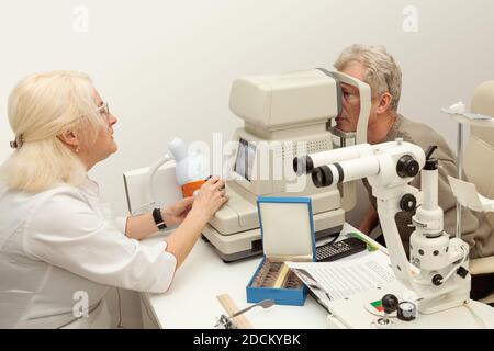 Il medico oftalmologo controlla la vista di un paziente anziano sul rifrattometro moderno Foto Stock