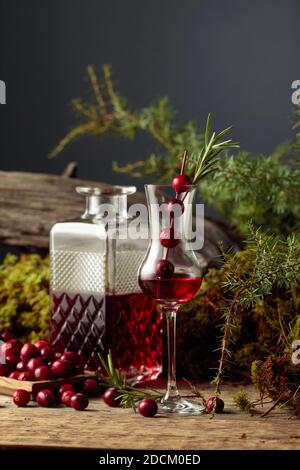 Mirtilli rossi e liquori di mirtilli su un vecchio tavolo di legno. Nello sfondo muschio, ramo di ginepro, e vecchio snag. Foto Stock