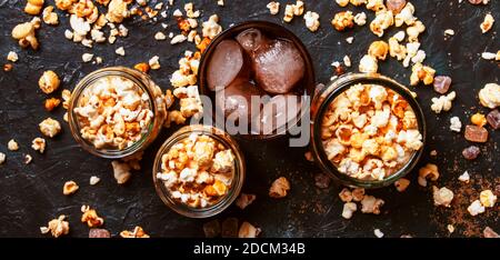 Cola ghiacciata e popcorn al caramello, cibi e bevande malsani, tavolo nero, vista dall'alto Foto Stock