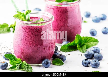 Yogurt o frullati porpora fatti in casa con mirtilli, semi di chia e foglie di menta in vasi di vetro su sfondo grigio, fuoco selettivo Foto Stock