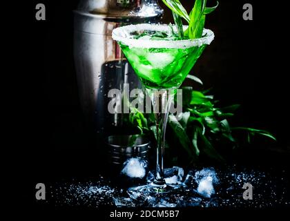 Cocktail alcolico verde con ghiaccio in un bicchiere martini decorato con zucchero, fondo nero, fuoco selettivo Foto Stock