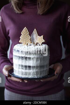 Le mani femminili tengono una torta di Natale fatta in casa decorata con biscotti di pan di zenzero. Foto Stock