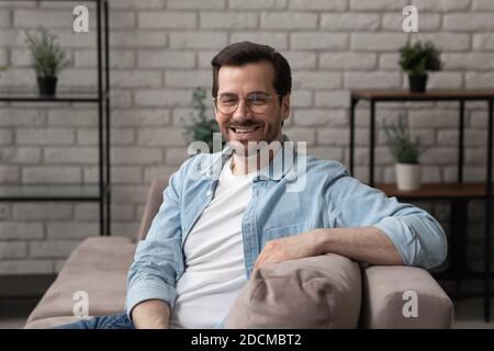 Ritratto di sorridente giovane 30s bell'uomo seduto sul divano. Foto Stock