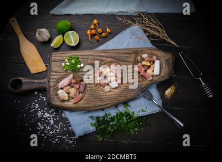 Misto di pesce crudo. Sfondo nero. Concetto di cibo. Cocktail di pesce surgelato con cipolle, cristalli di sale, aglio e lime su tavola di legno. Foto Stock