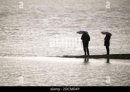 Wilhelmshaven, Germania. 22 novembre 2020. Due persone si ergono con ombrelloni su un molo di pietra sulla spiaggia sud e si affacciano sul Mare del Nord. Credit: Mohssen Assanimoghaddam/dpa/Alamy Live News Foto Stock