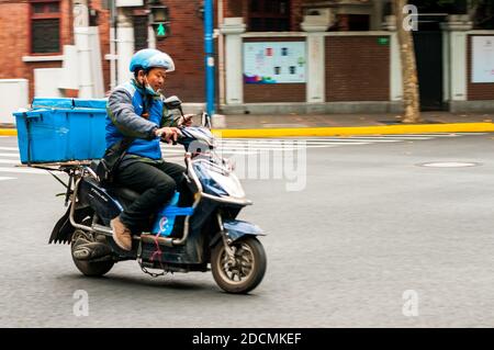 Un pilota di consegna Eleme che usa il suo telefono mentre guida il suo scooter all'incrocio tra le strade di Jiaozhou e Wuding nel distretto Jing'an di Shanghai. Foto Stock