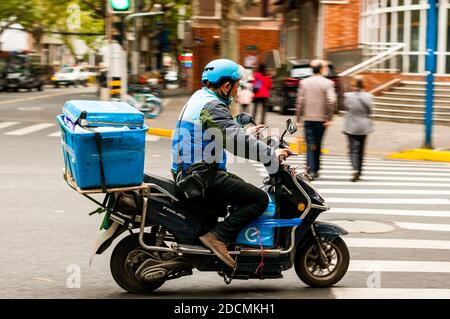 Un pilota di consegna Eleme che usa il suo telefono mentre guida il suo scooter all'incrocio tra le strade di Jiaozhou e Wuding nel distretto Jing'an di Shanghai. Foto Stock