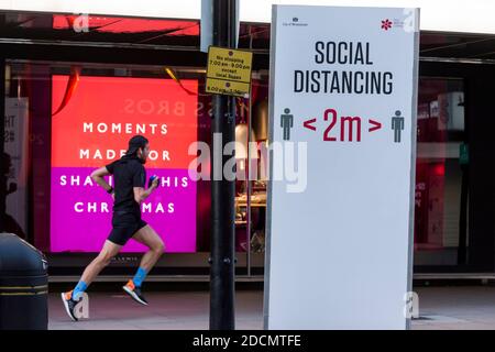 Londra, Regno Unito. 22 novembre 2020. Un runner passa davanti a un cartello di distanza sociale e a una vetrina decorata del grande magazzino John Lewis su Oxford Street. Il governo del Regno Unito dovrebbe allentare alcune restrizioni di blocco pandemiche di coronavirus il 2 dicembre in Inghilterra nel periodo fino a Natale. Credit: Stephen Chung / Alamy Live News Foto Stock