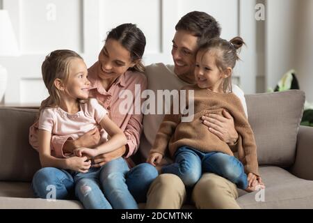 Le piccole figlie si siedono sui giri dei genitori che parlano riposandosi sul divano Foto Stock