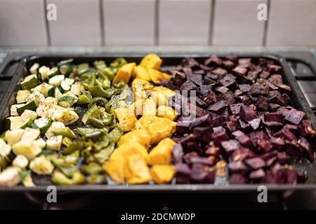 Primo piano di verdure cotte al forno su vassoio da forno nero pepperoni verdi a fette, patate dolci gialle, barbabietole, zuchinni verdi con spezie e pepe. Foto Stock